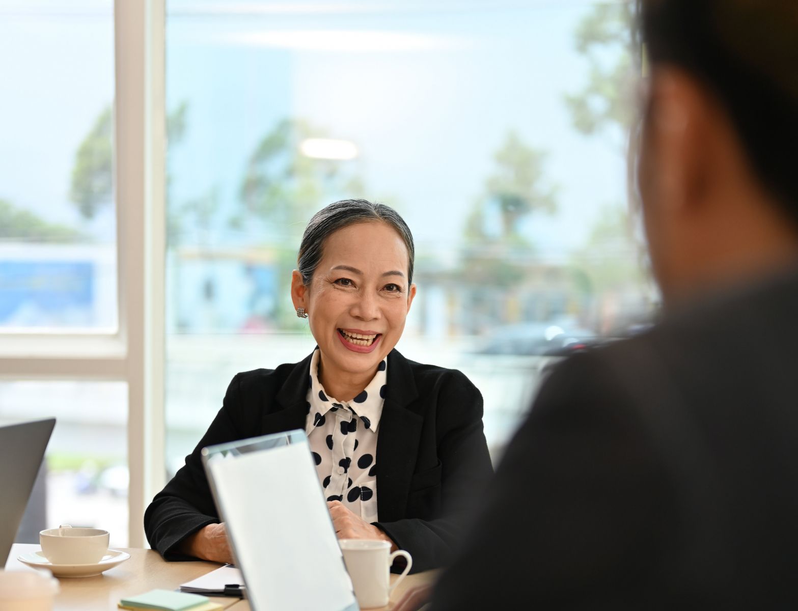 a woman sitting at a table with her Certified Financial planner, smiling, feeling secure with her financial future. 