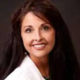 A woman with long dark hair, wearing a white top, smiles at the camera against a dark background—she exudes the confidence of an experienced financial advisor.