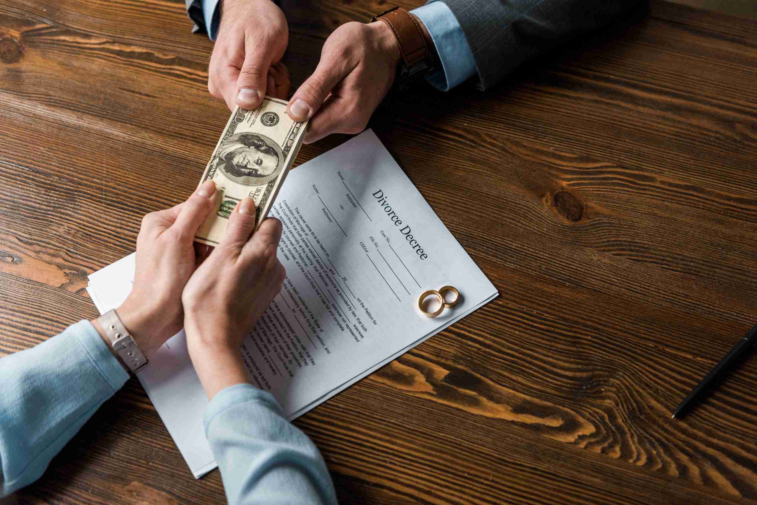 Husband and wife fighting for money above a divorce decree document and two wedding rings, the difficult financial aspects of divorce.