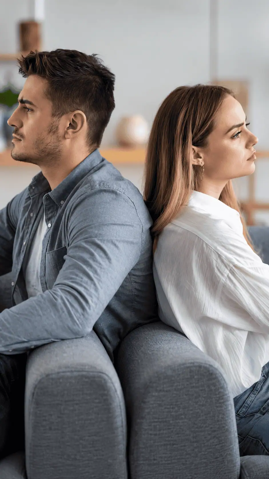 A man and a woman sitting back-to-back on a sofa, looking in opposite directions.